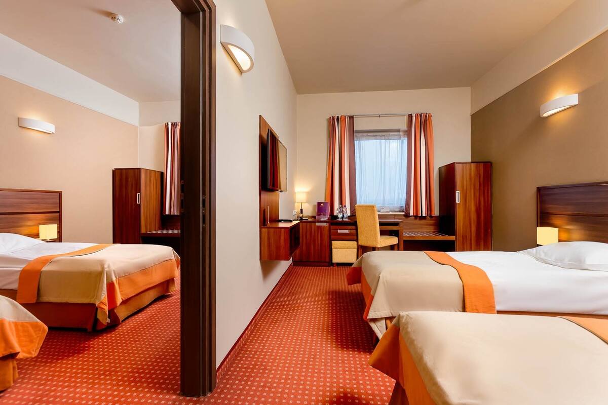 A hotel room with two beds, a desk, a chair, and a wardrobe.
