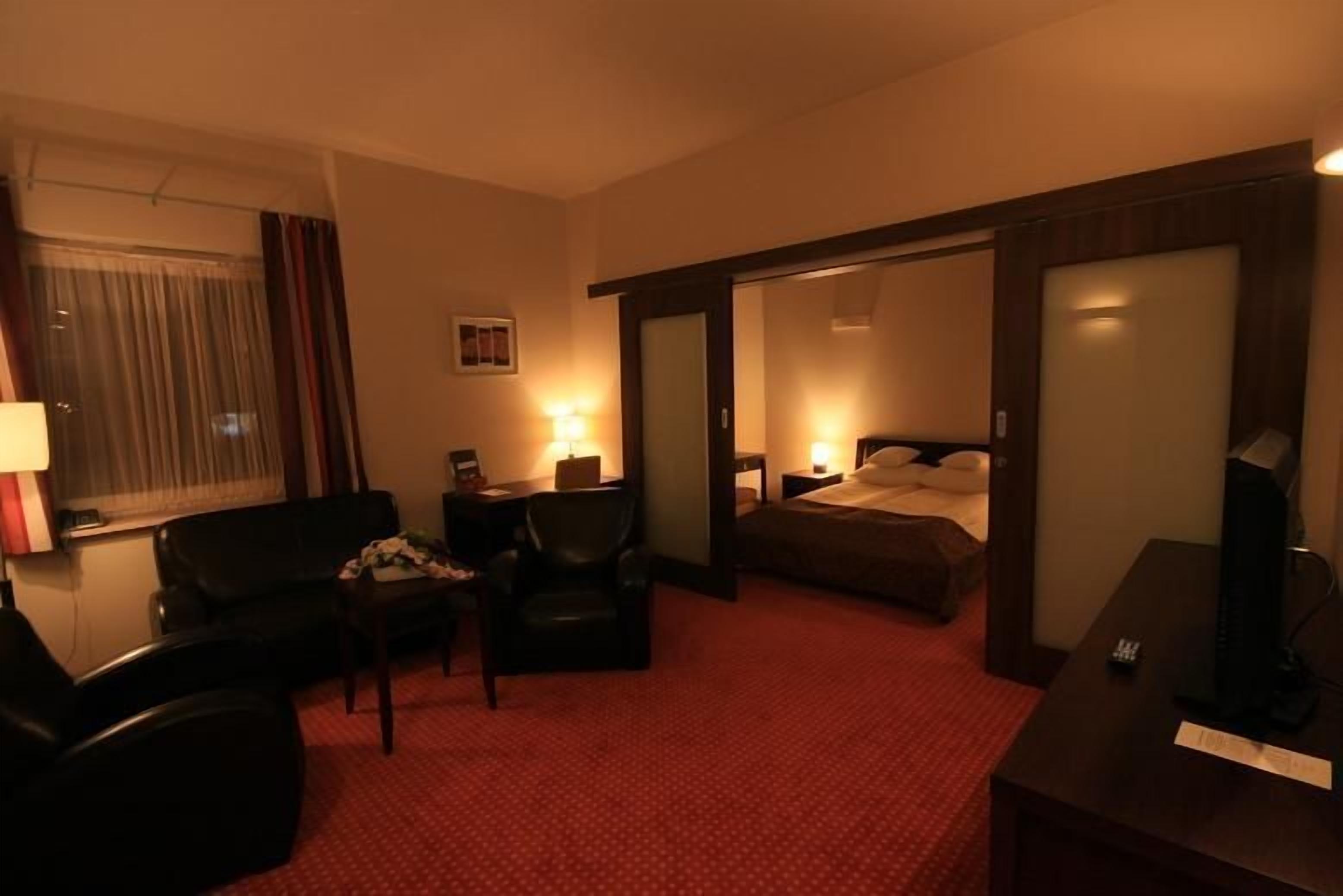 Habitación de hotel con cama, escritorio, silla, televisión y ventana con cortinas.