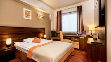 A hotel room with a large bed, a desk with a computer, a TV, and a window with curtains.