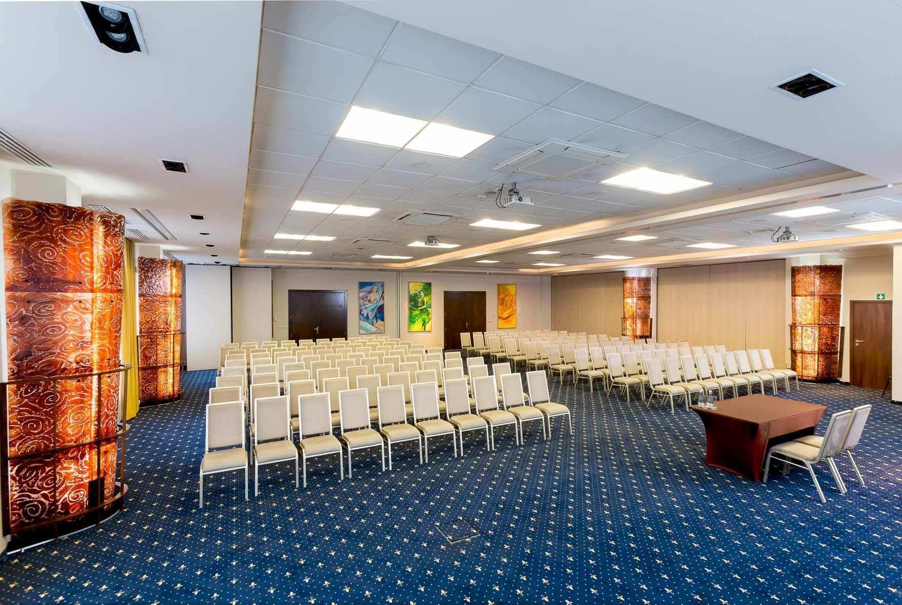 A conference room with rows of chairs, a projector, and a carpeted floor.