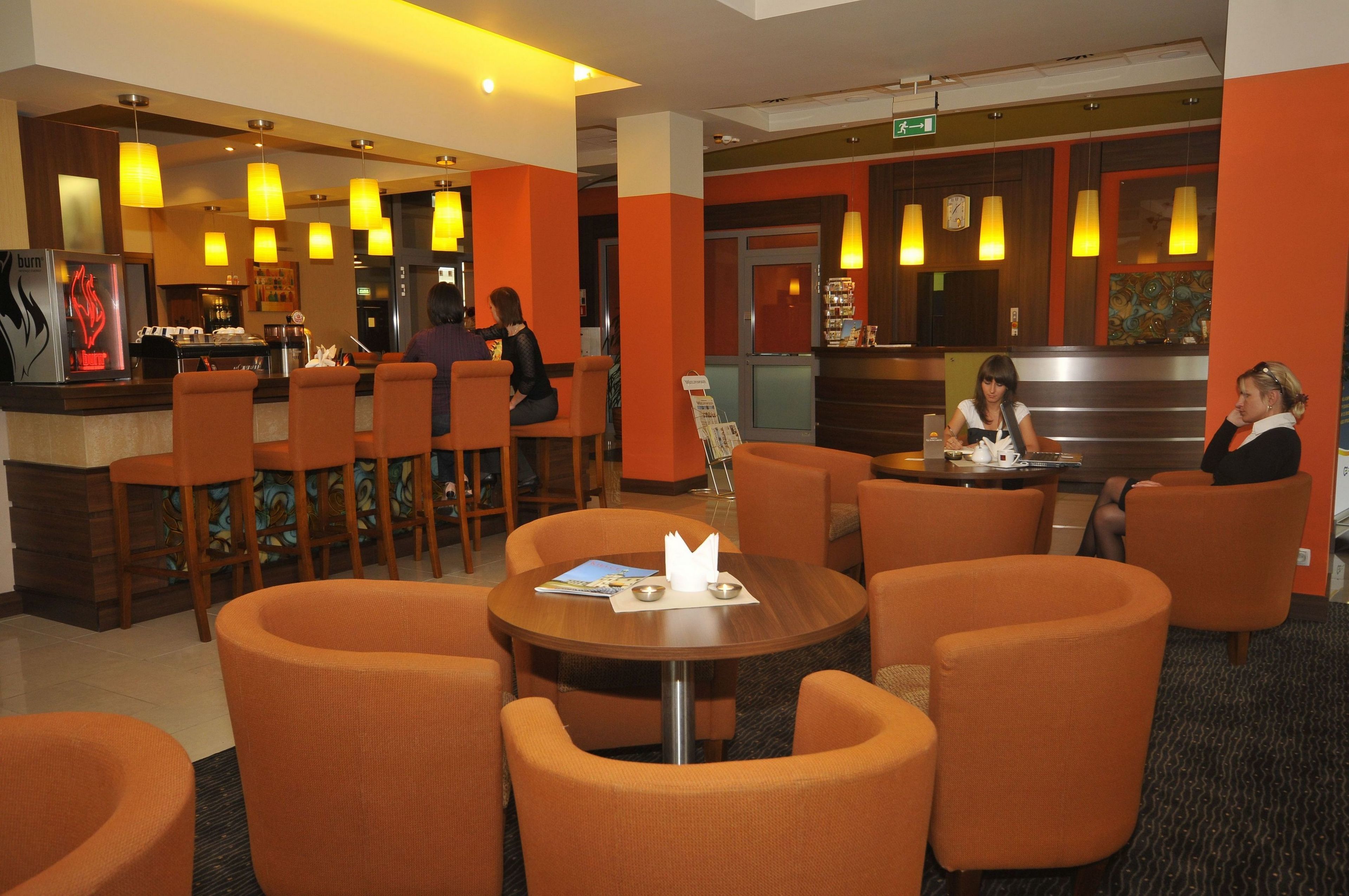 A hotel lobby with orange chairs, a coffee bar, and a reception area.