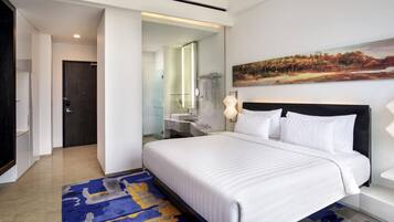 Una habitación de hotel moderna con una cama grande, un baño con puerta de vidrio y un cuadro en la pared.