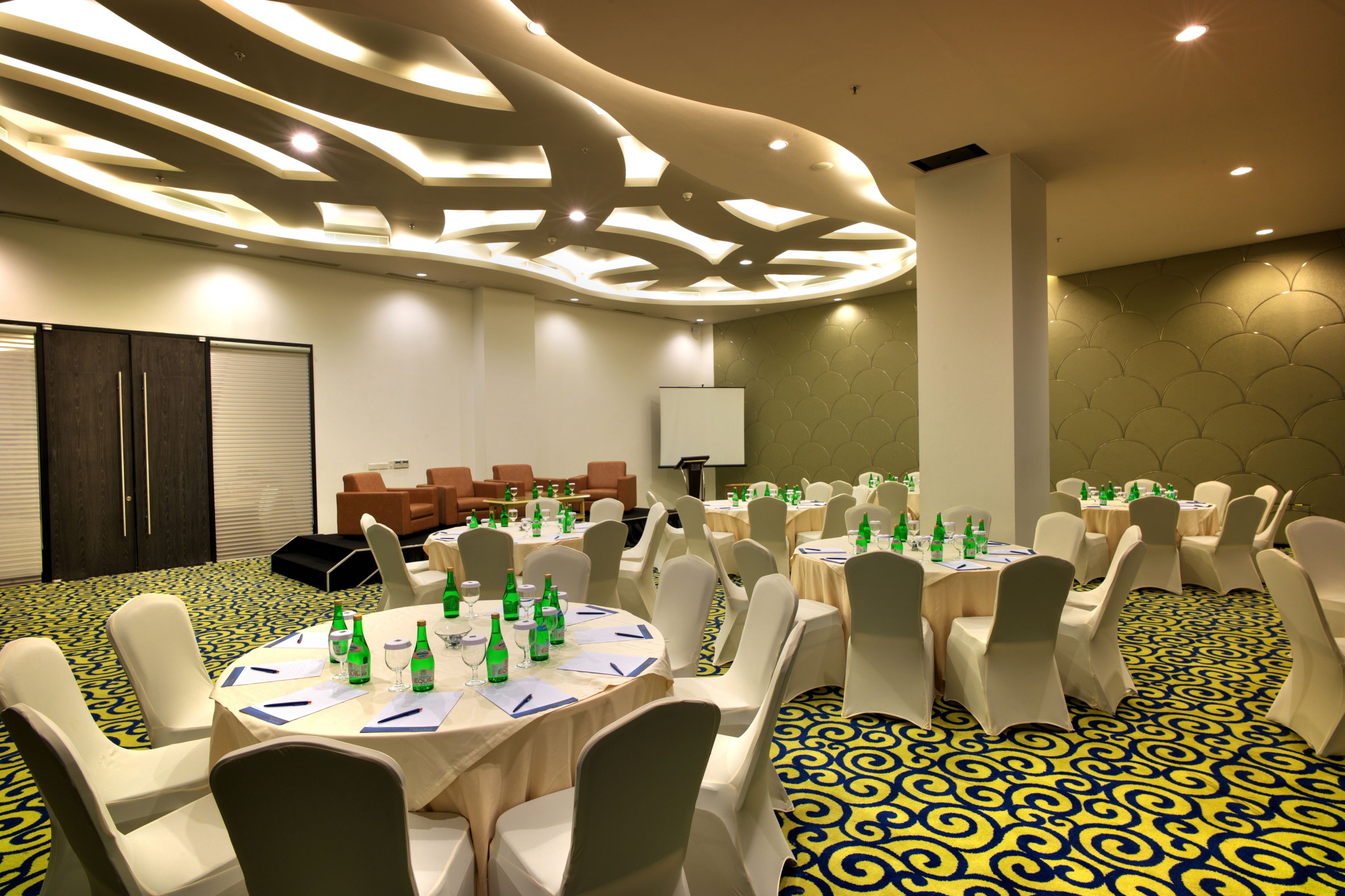 A conference room with round tables, white chairs, and a patterned carpet.