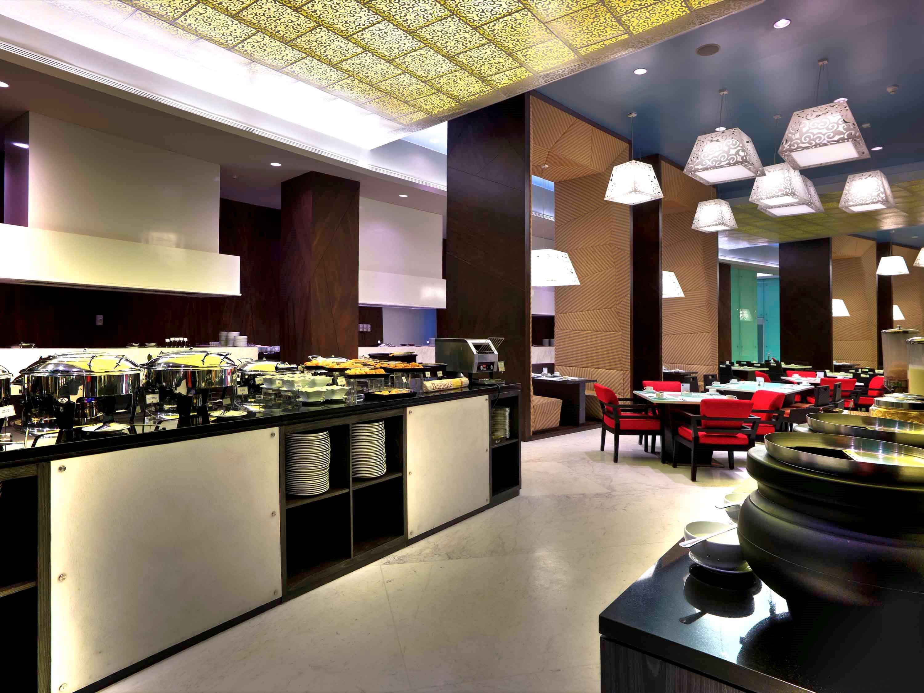 Un comedor moderno de hotel con mesas de buffet, disposición de mesas y iluminación decorativa.