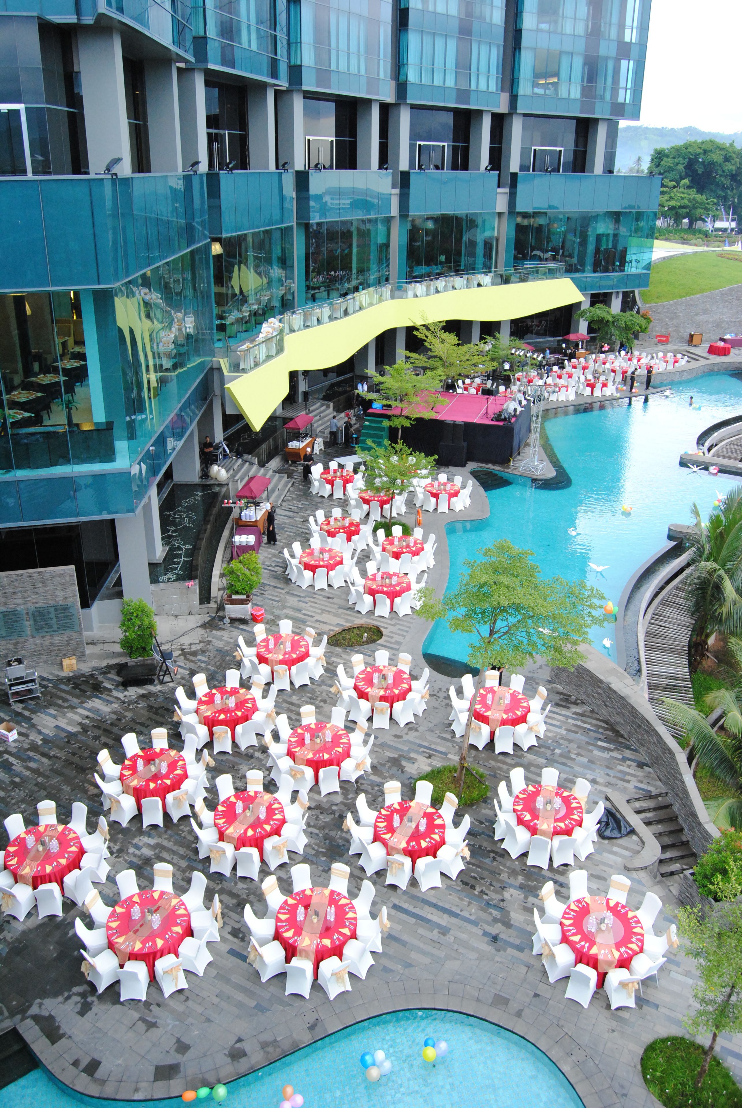 A hotel with outdoor dining areas, a swimming pool, and a modern building with balconies.
