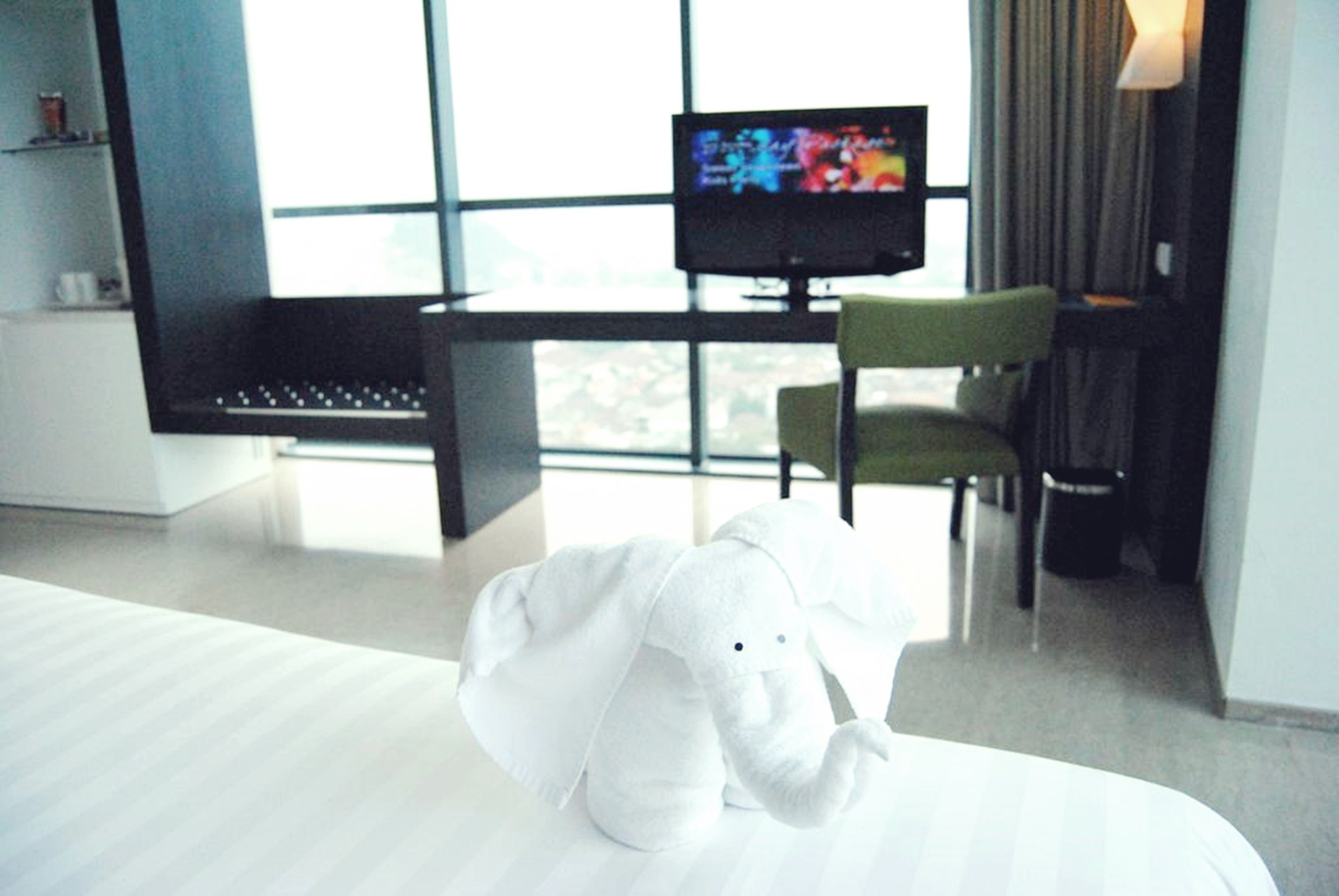 A hotel room with a bed, a television on a stand, a green chair, and a window with a view.