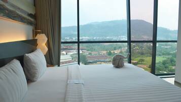 Una habitación de hotel con un ventanal grande, una cama, una lámpara y un cuadro en la pared.