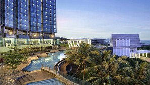 A modern hotel with a large pool area, palm trees, and a view of the ocean. - Novotel Lampung (Bandar Lampung)
