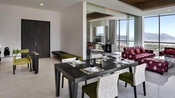 A modern dining area with a dark wooden table, green and patterned chairs, and a seating area with red patterned sofas.