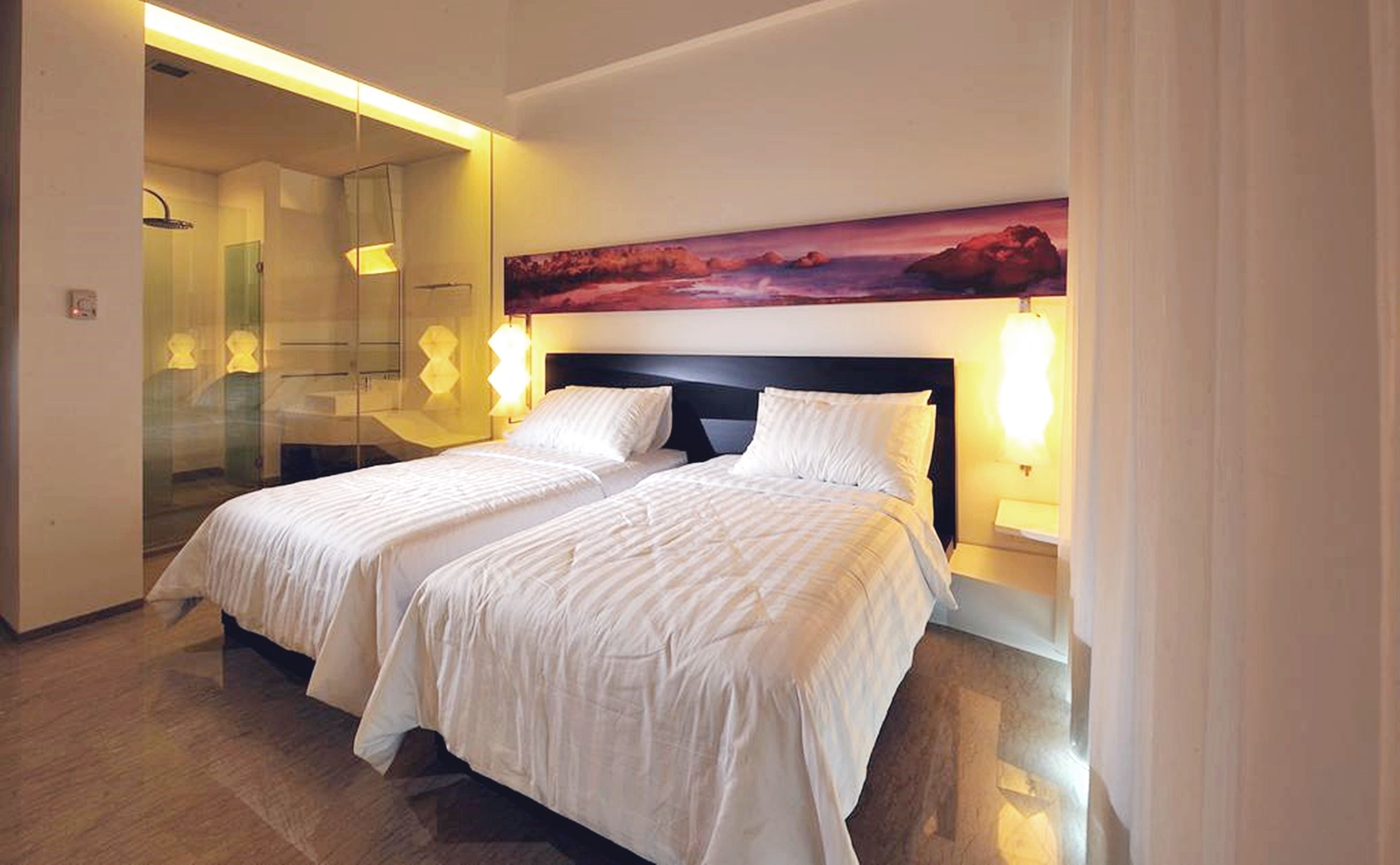 A hotel room with two beds, a large painting above the beds, and a glass shower area.
