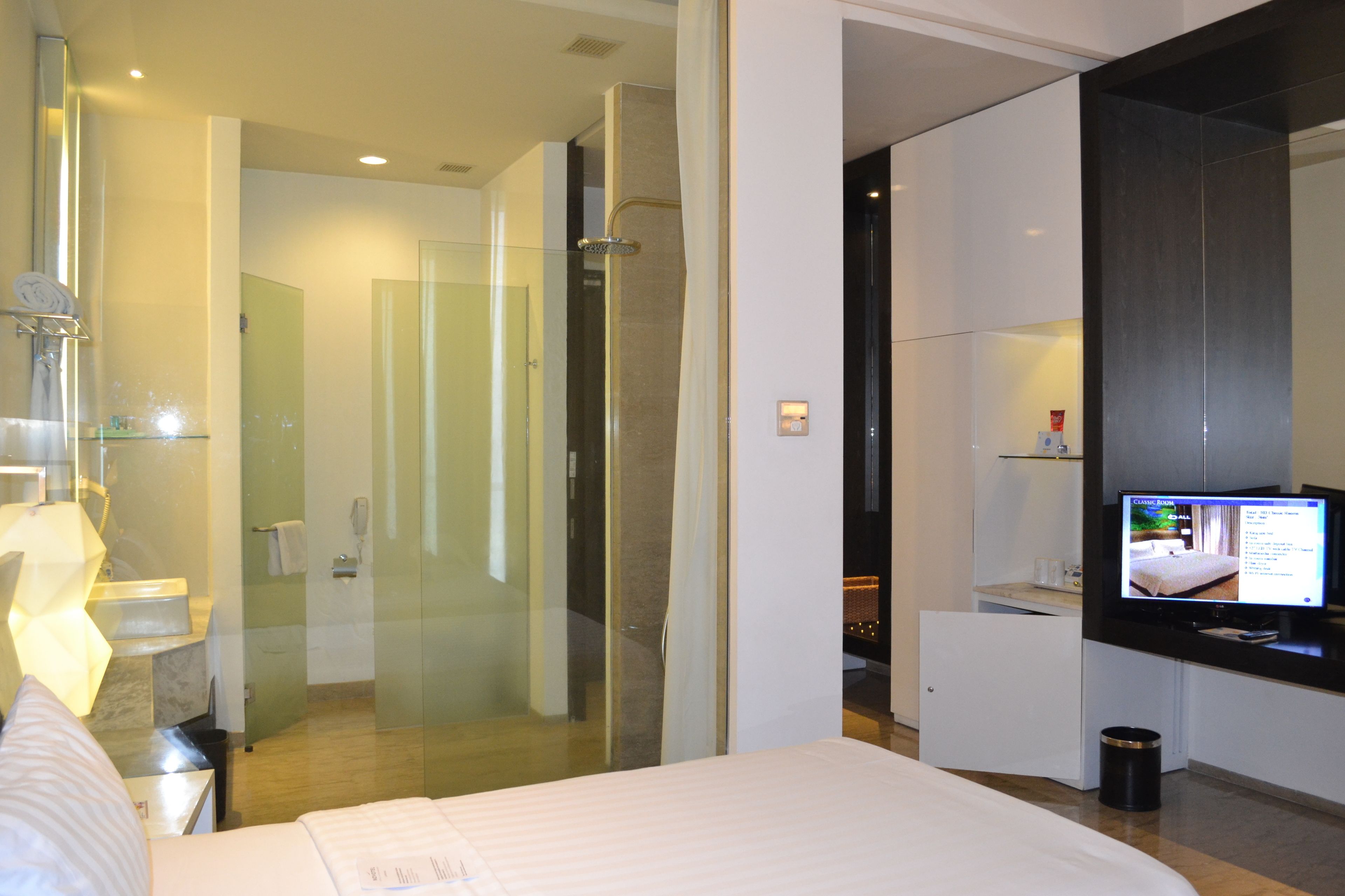 Una habitación de hotel moderna con una cama grande, cabina de ducha de vidrio, televisor y minibar.
