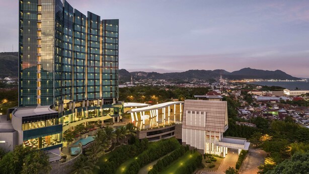 A modern hotel with a prominent 'Novotel' sign, featuring a rooftop pool and lush landscaping. - Novotel Lampung (Bandar Lampung)