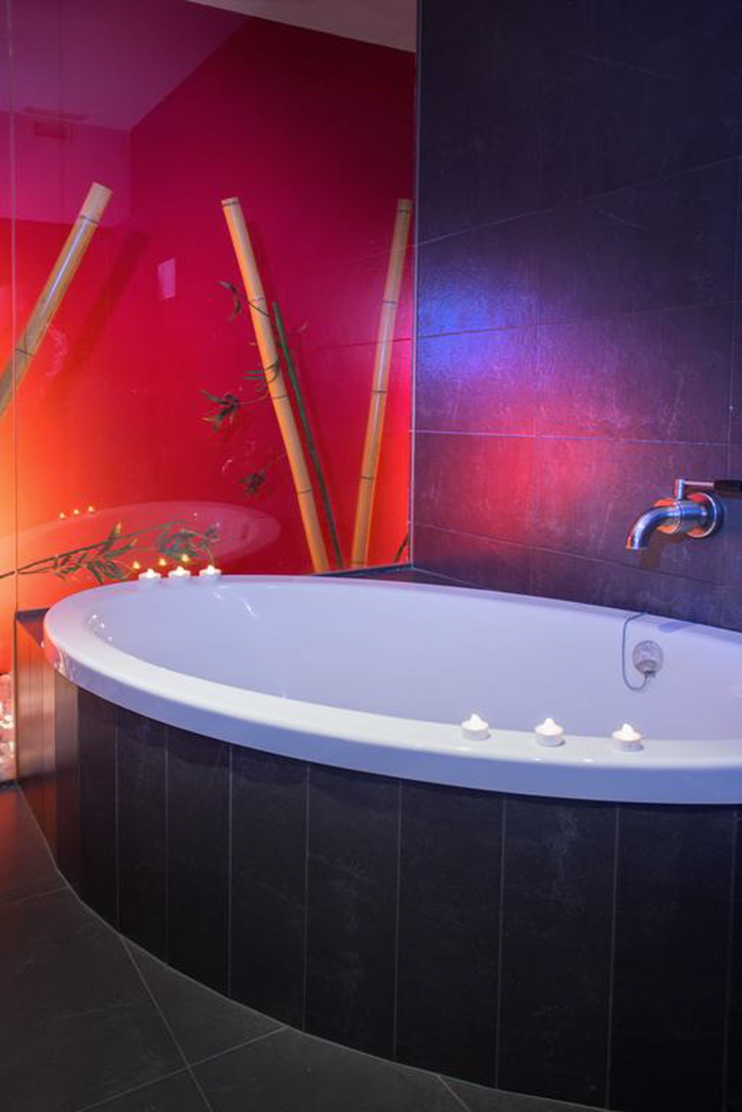 A modern bathroom with a freestanding bathtub, dark tiled walls, and bamboo decor.