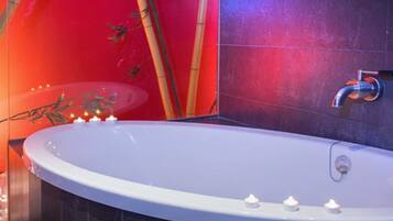 A modern bathroom with a freestanding bathtub, dark tiled walls, and bamboo decor.