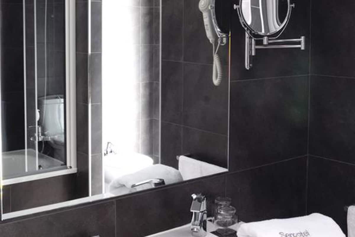 A modern bathroom with a large mirror, a handheld hair dryer, and a sink with toiletries.