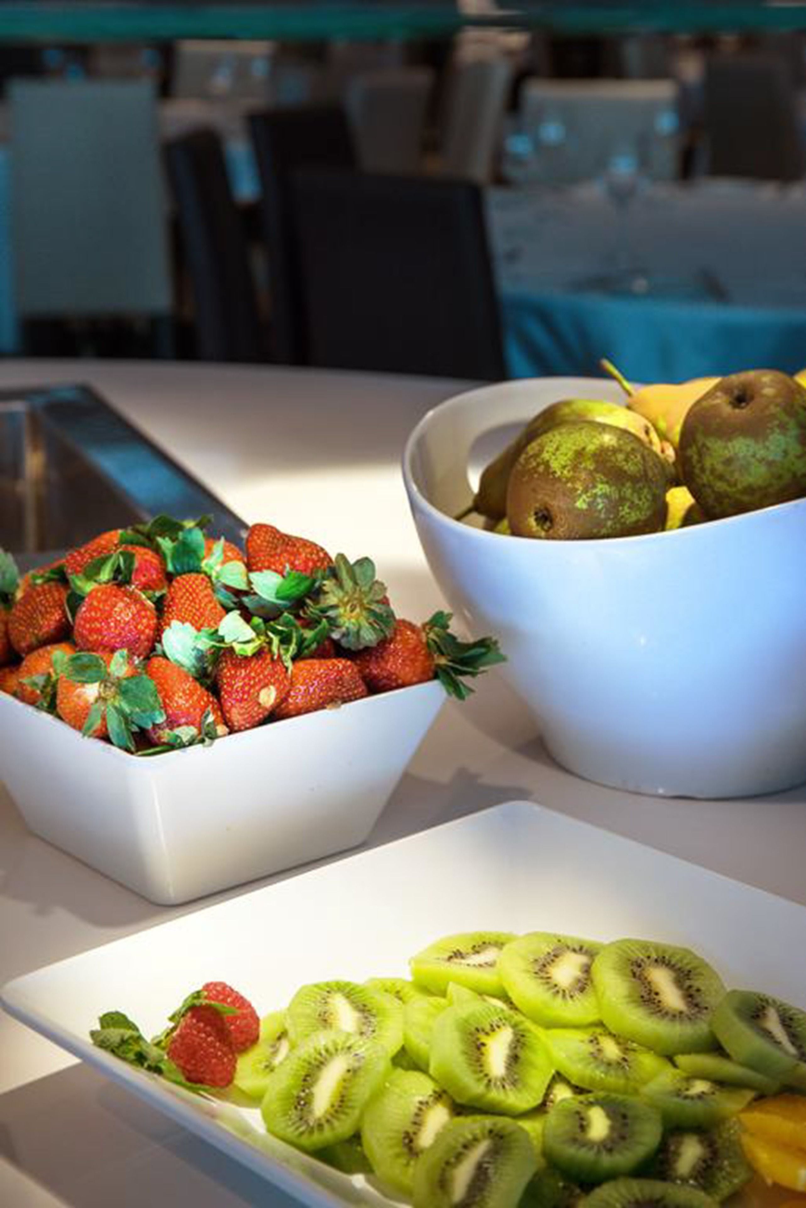 A buffet table with bowls of strawberries, kiwis, and pears.