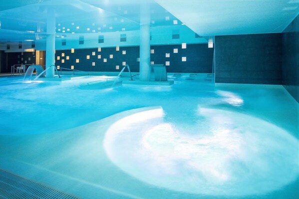 Una piscina interior con un diseño moderno, que presenta patrones geométricos en las paredes y una columna central.