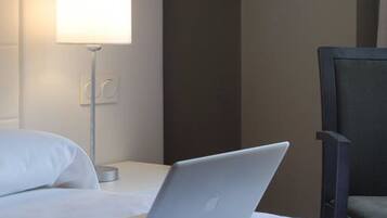 A hotel room with a bed, a laptop, a bedside lamp, and a chair.