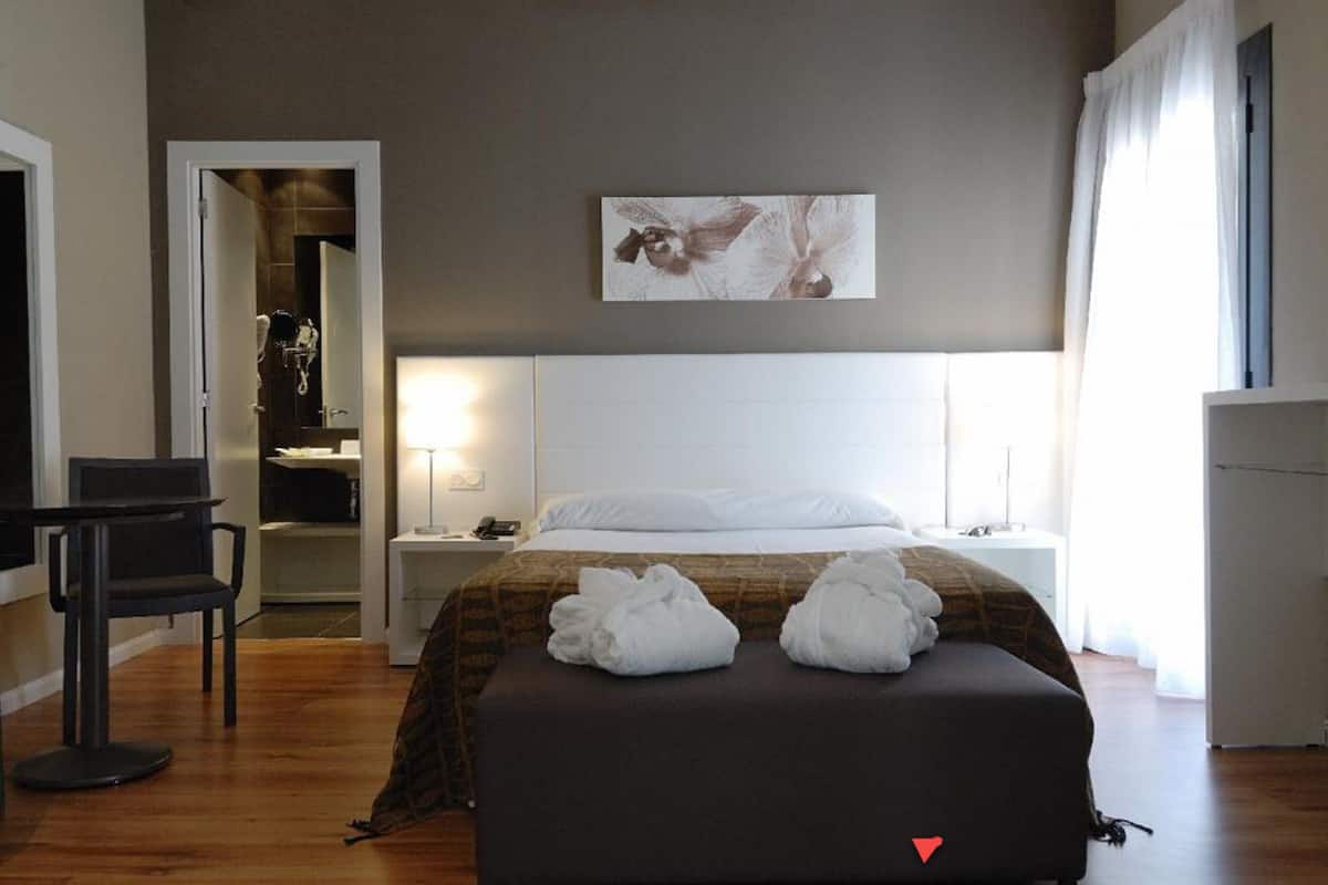 A hotel room with a bed, a desk, a chair, a bedside table, and a wall-mounted artwork.