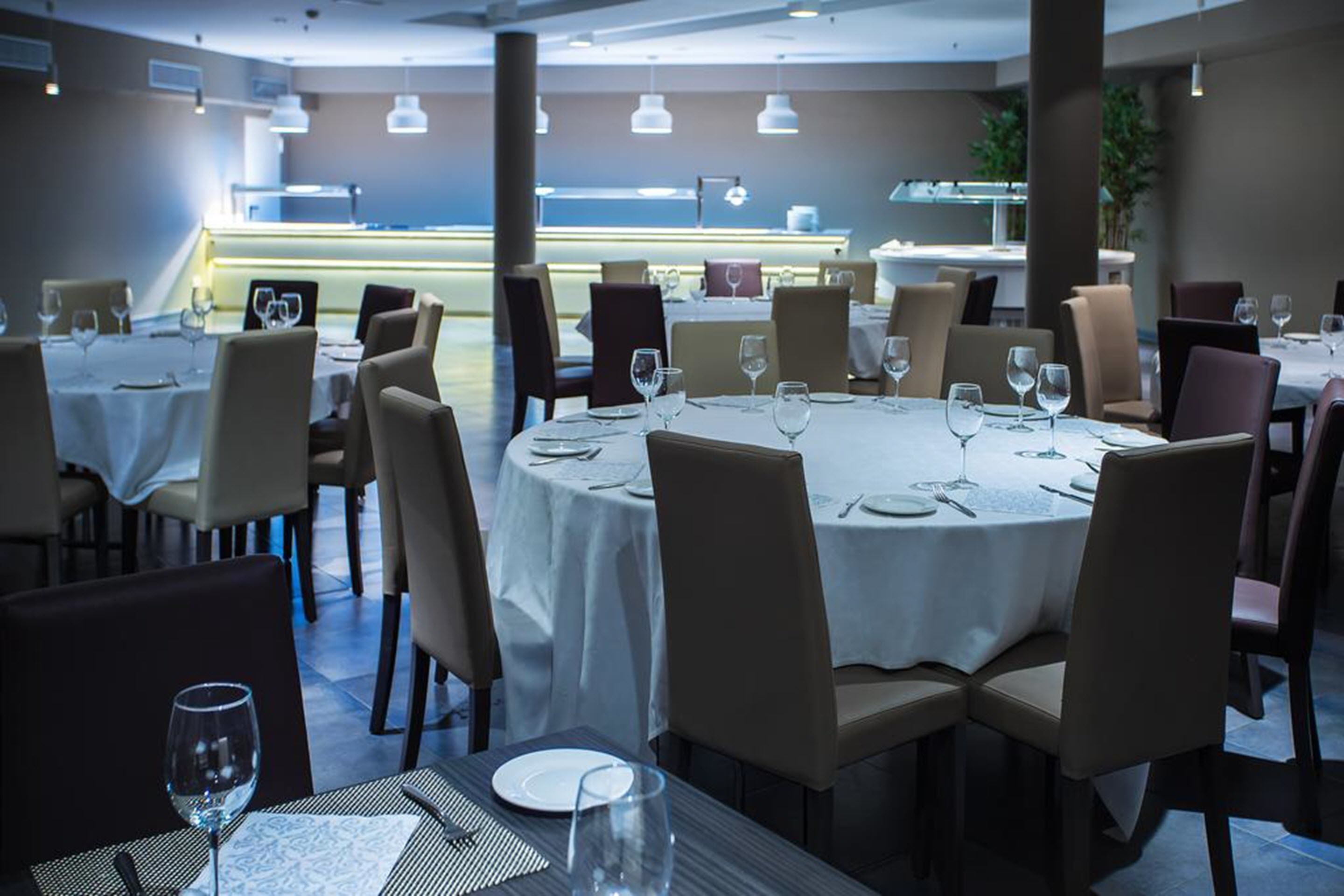 A restaurant with round tables, beige chairs, and white tablecloths.