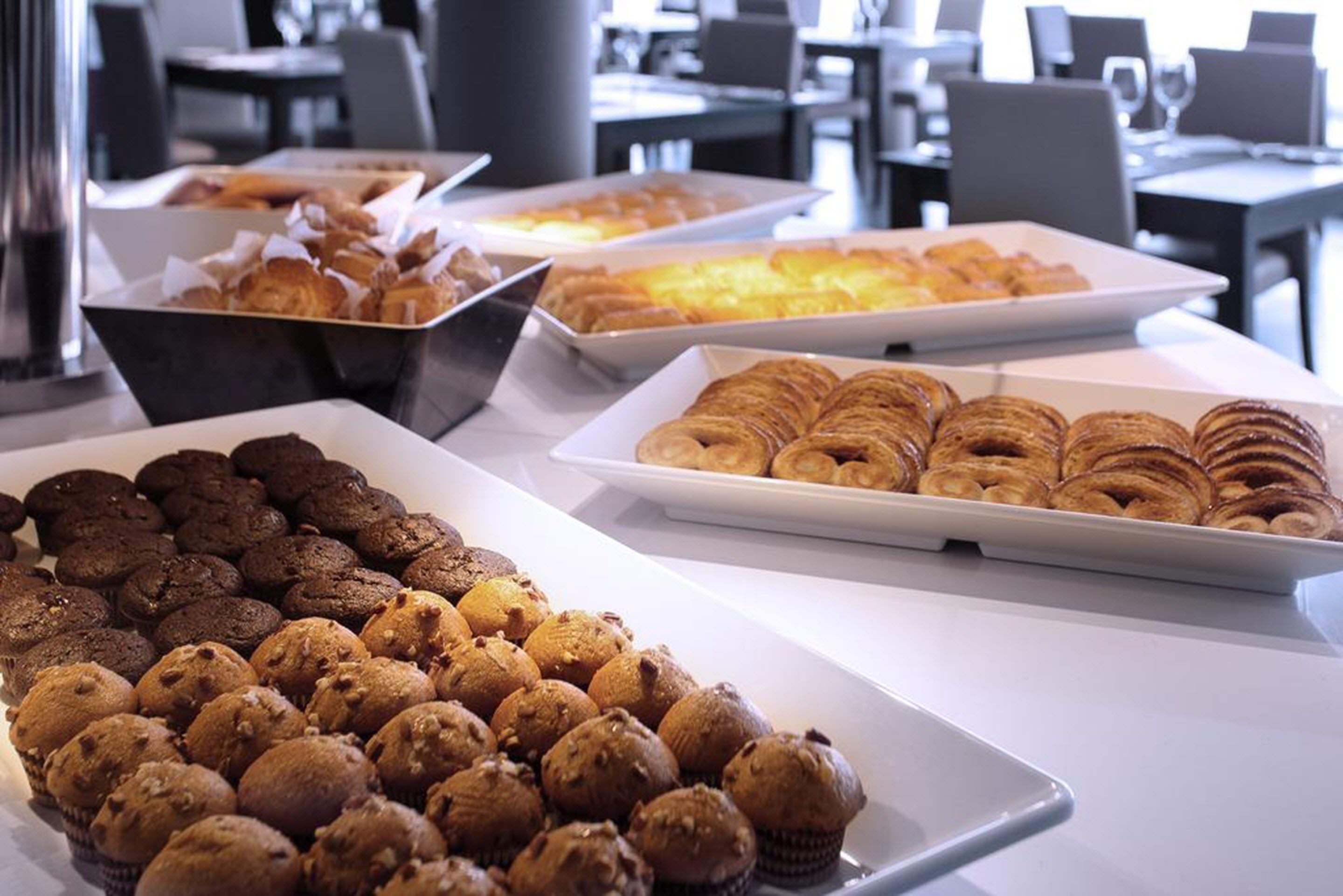 Una mesa de buffet con diversas opciones de repostería, incluyendo muffins, croissants y pasteles.