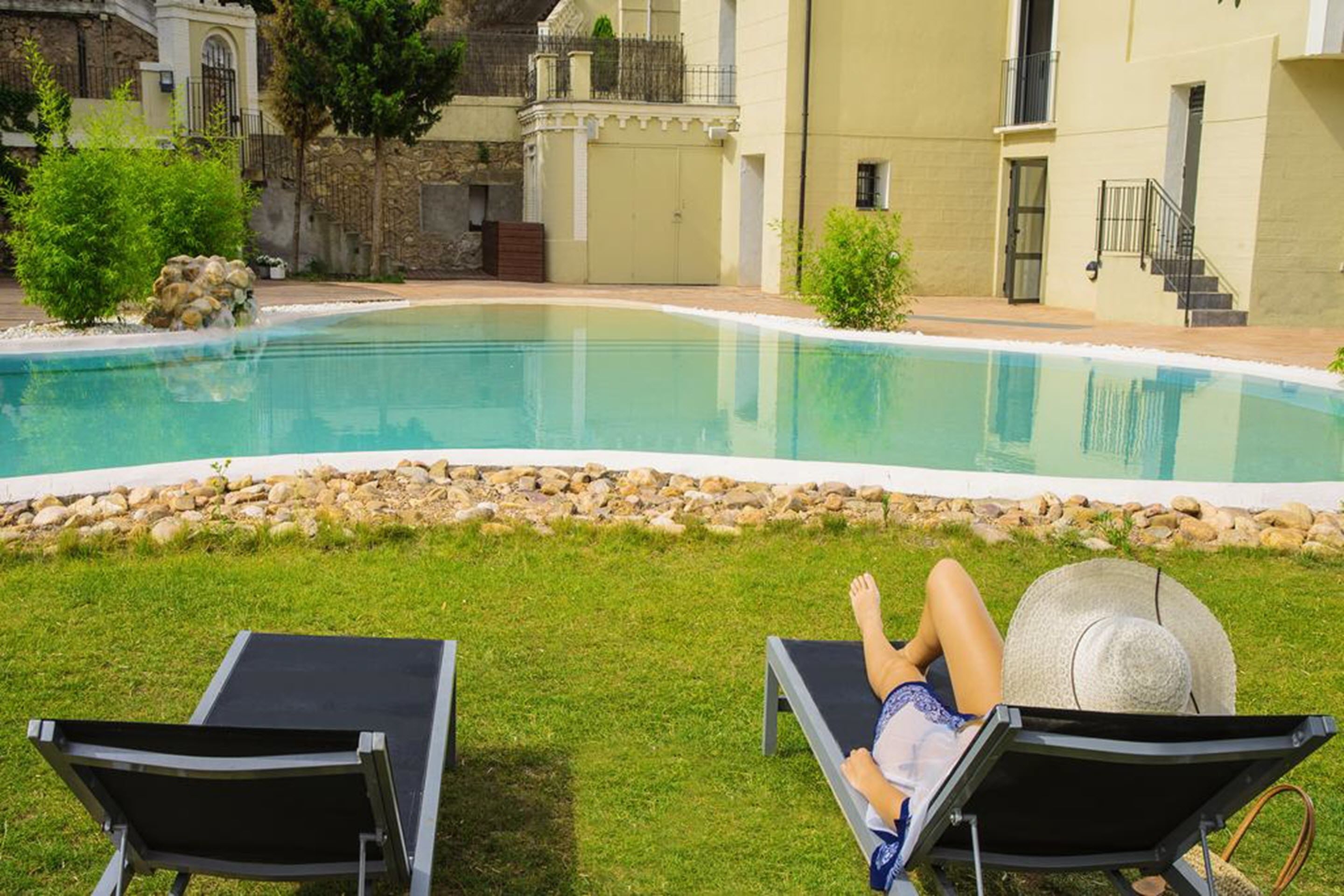 Piscina con dos sillas reclinables y una persona relajándose.