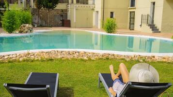 Piscina con dos sillas reclinables y una persona relajándose.