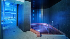 A modern indoor swimming pool with a glass barrier, a red and white tiled edge, and a view of a building through the entrance. - Hotel Balneario Alhama de Aragon (Alhama de Aragon)