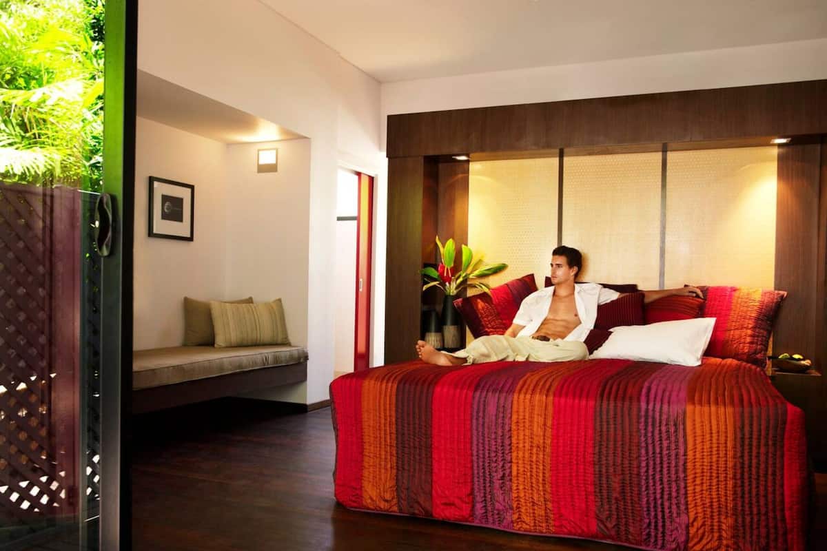 A modern bedroom with a large bed, a bedside table, a small sofa, and a potted plant.