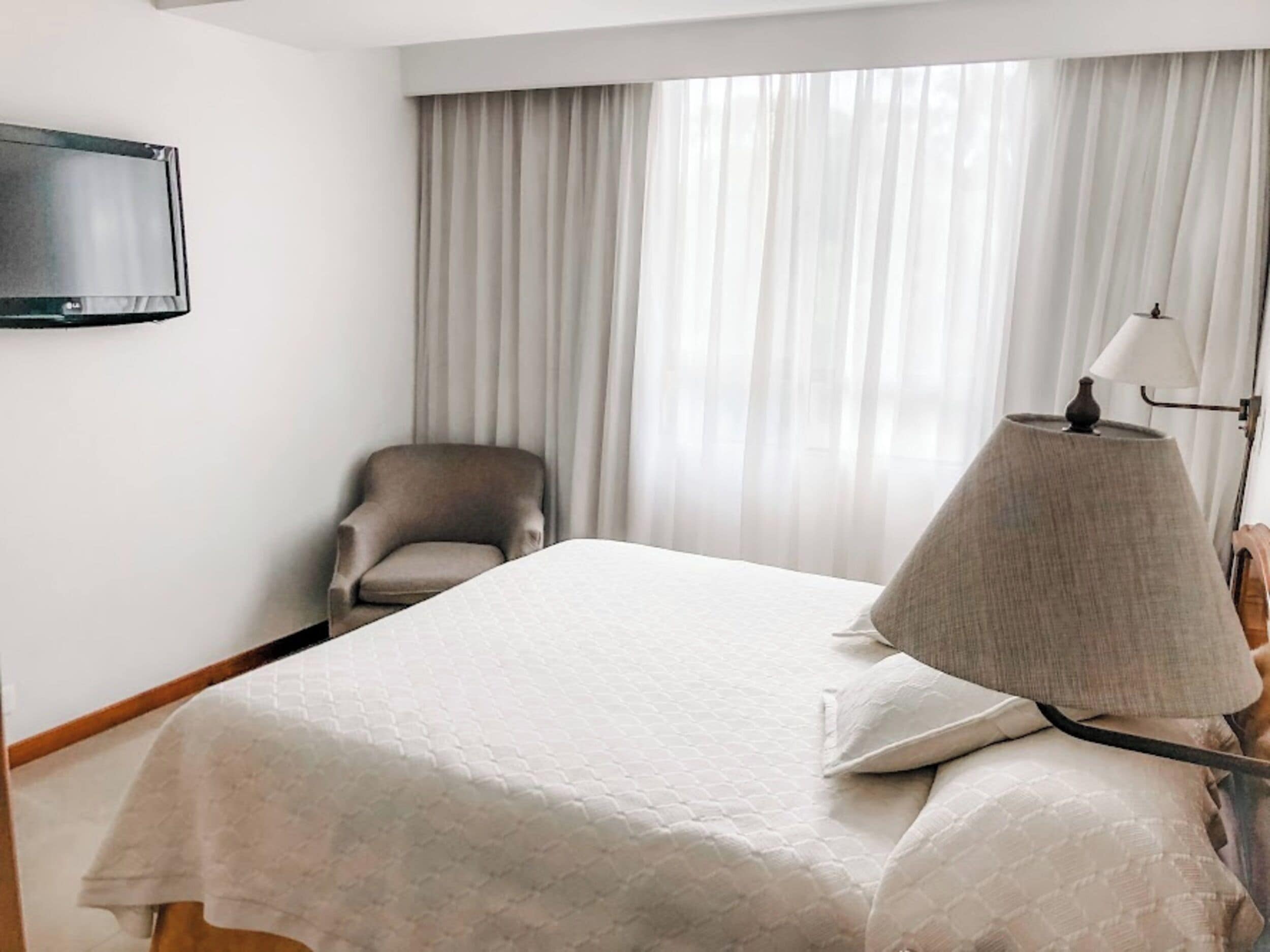 Et hotelværelse med en seng, en stol, et fjernsyn ophængt på væggen og en lampe.