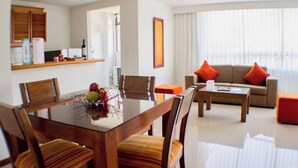 A modern hotel room with a dining area, a sofa set, and a kitchen area.
