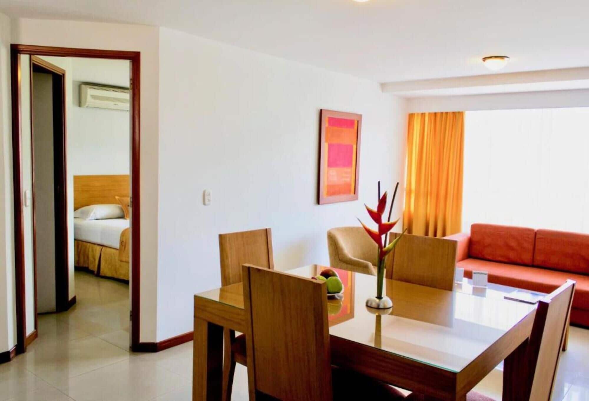 Uma sala de estar moderna com uma mesa de jantar de vidro, cadeiras de madeira, um sofá vermelho e um quadro na parede.