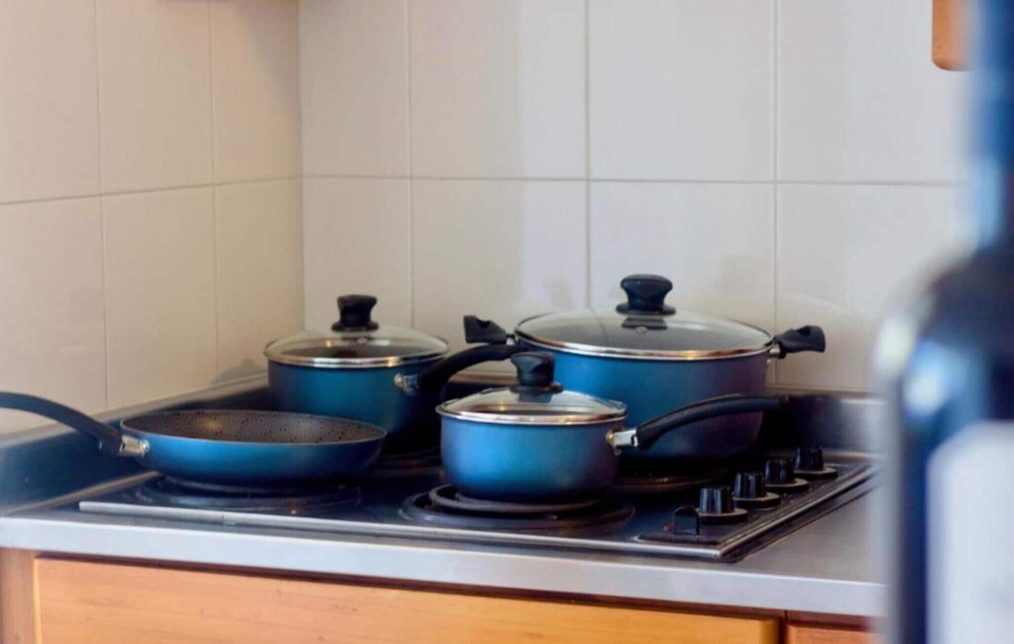 A kitchen with a gas stove, three blue pots, and a frying pan.
