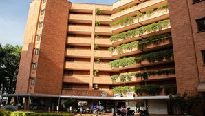 A multi-story building with a brick facade, multiple balconies with greenery, and a sign indicating a business or commercial use.