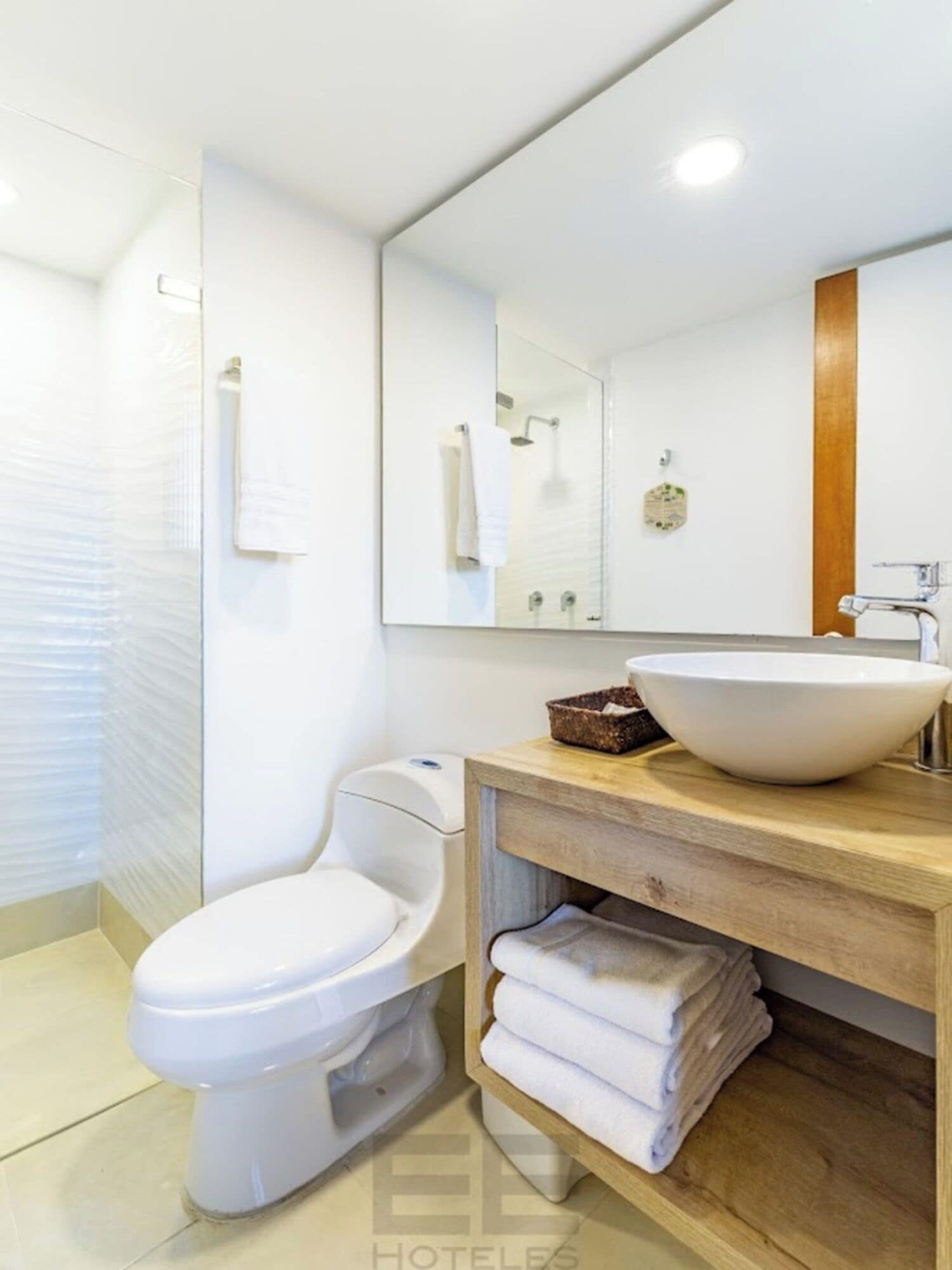 A modern bathroom with a white toilet, a wooden vanity with a large sink, and a mirror above the vanity.