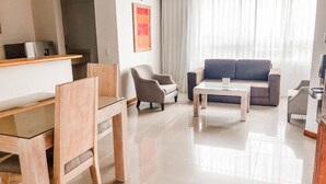 A modern living room with a sofa, armchairs, a coffee table, and a dining area with chairs and a table.