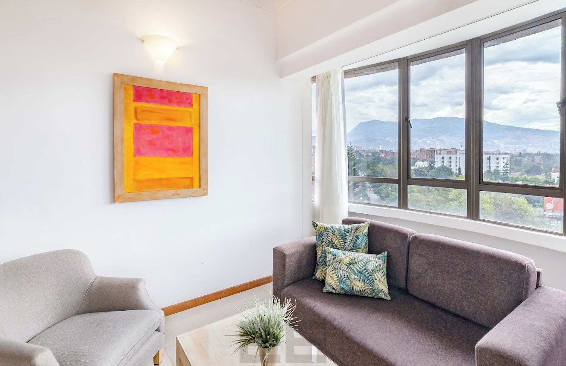 Una sala de estar con un sofá, un sillón, un cuadro y un ventanal con vista a la ciudad.