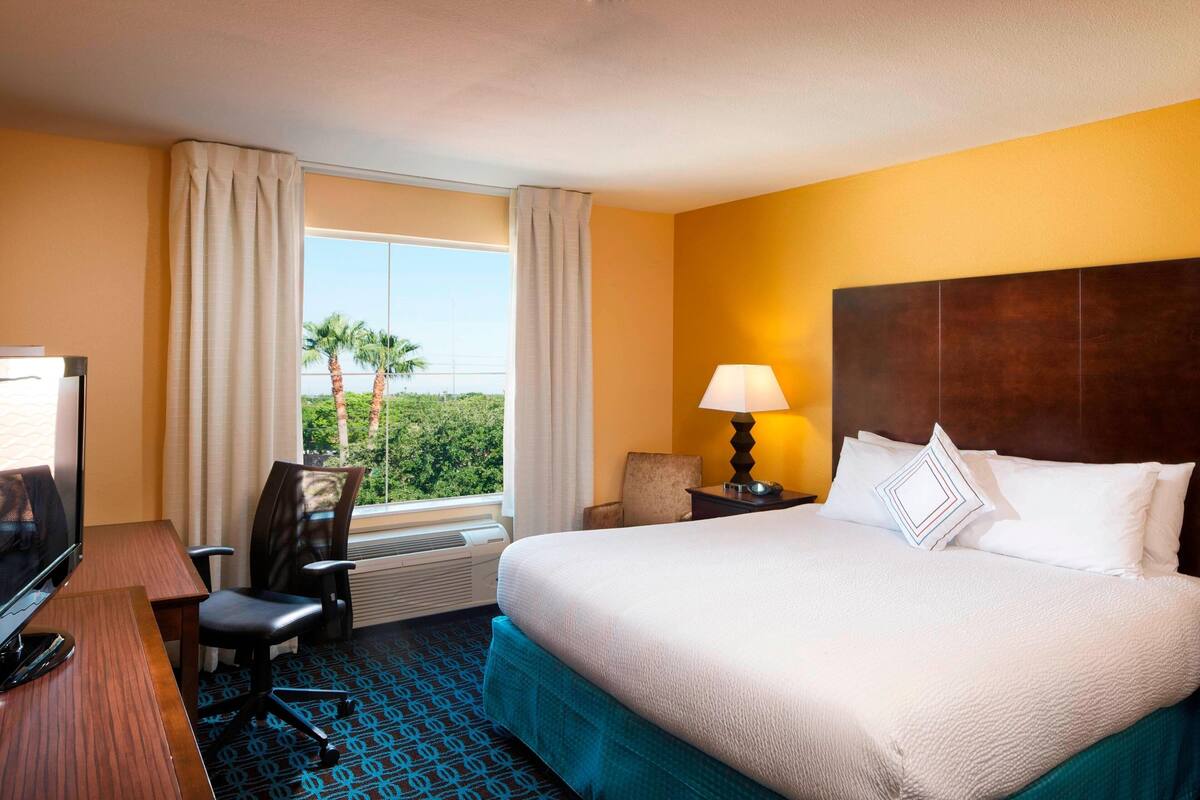 A hotel room with a bed, a desk, a chair, a TV, and a window with curtains.