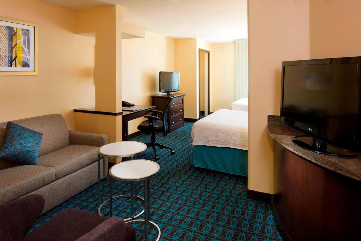 A hotel room with a sofa, a small round table, a bed, a TV, and a desk with a chair.
