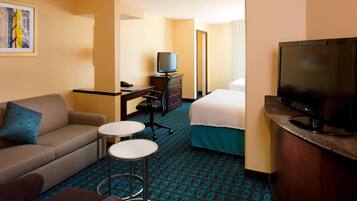 A hotel room with a sofa, a small round table, a bed, a TV, and a desk with a chair.