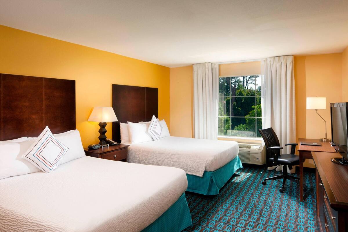 A hotel room with two beds, a desk, a chair, a TV, and a window with curtains.