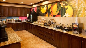 A kitchen area with a buffet setup, including a coffee machine, various food containers, and a waffle station.