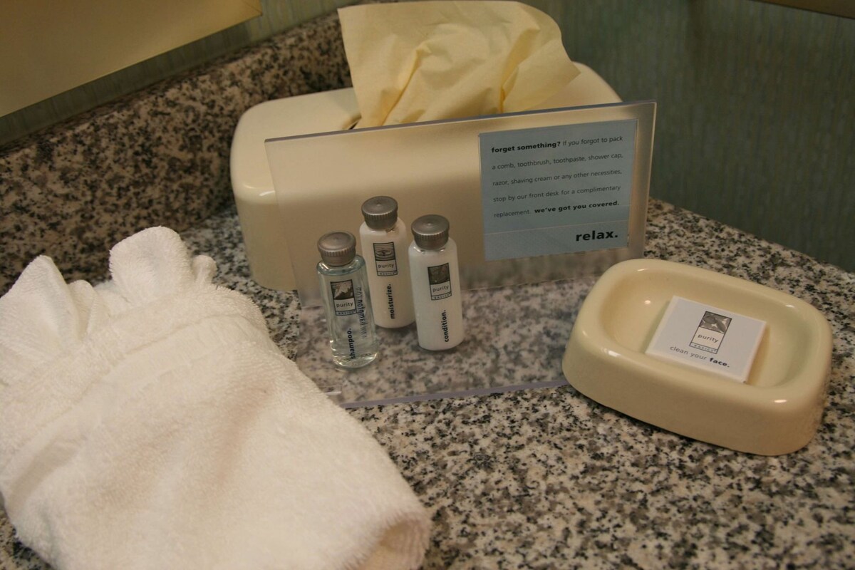A bathroom with a tissue box, three bottles of toiletries, a towel, and a soap dish.