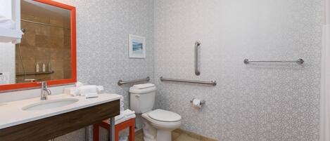 Un bagno moderno con lavandino bianco, water e doccia. Sono presenti mancorrenti alle pareti per sostegno.