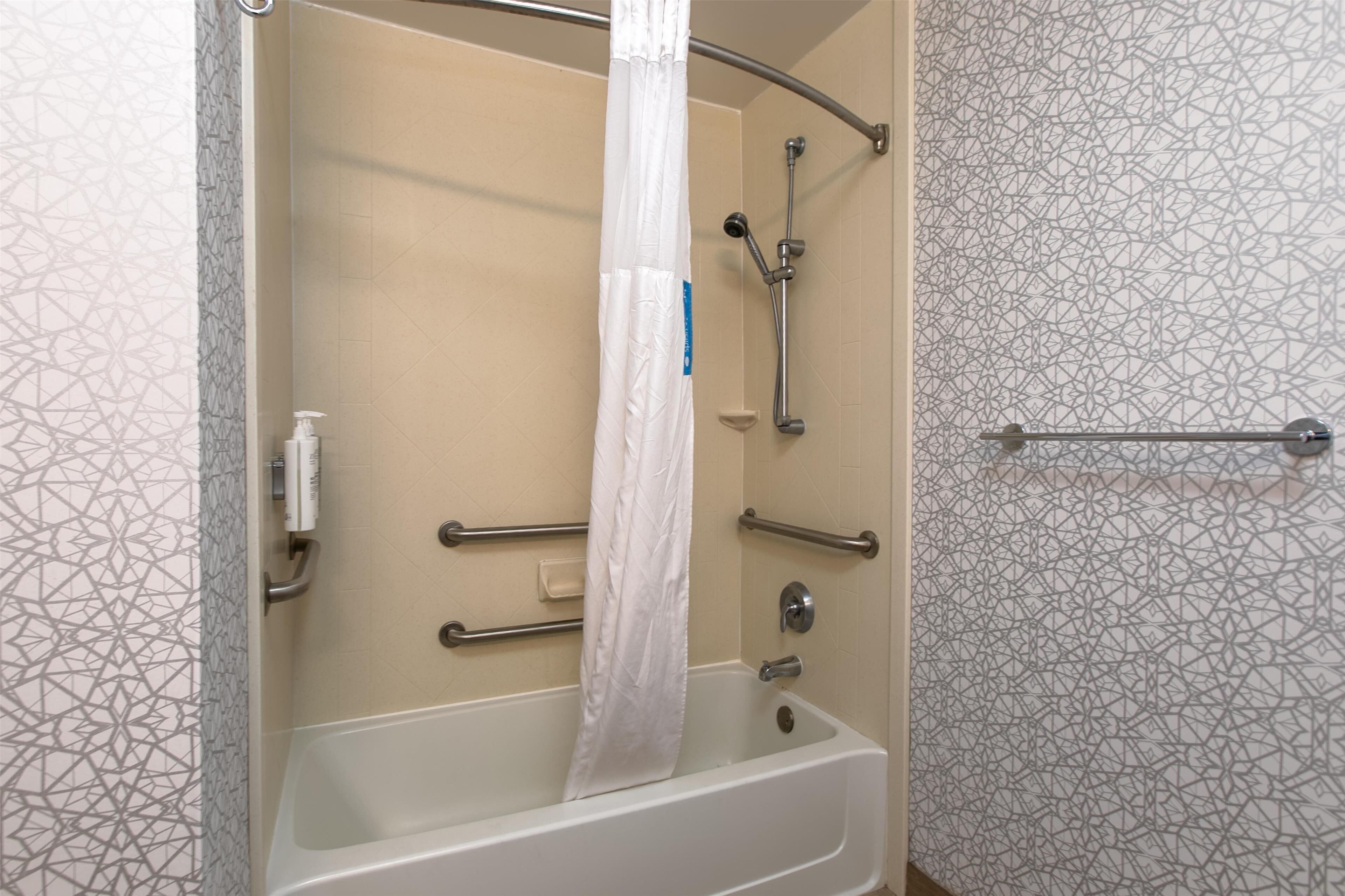 Eine Dusche mit weißem Vorhang, Duschbrause und Reinigungsbürste.