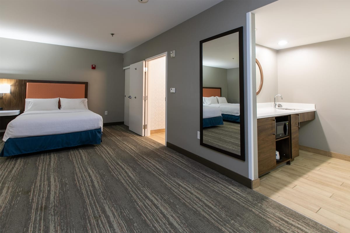 A hotel room with a bed, a bathroom with a sink, and a mirror.