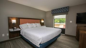 A hotel room with a large bed, bedside lamps, a telephone, a TV, and a window with a view of greenery.