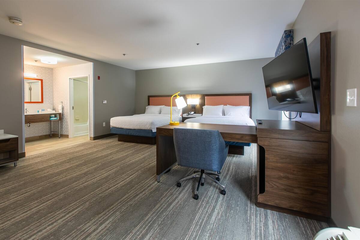 A hotel room with a bed, desk, chair, TV, and a bathroom visible through an open door.