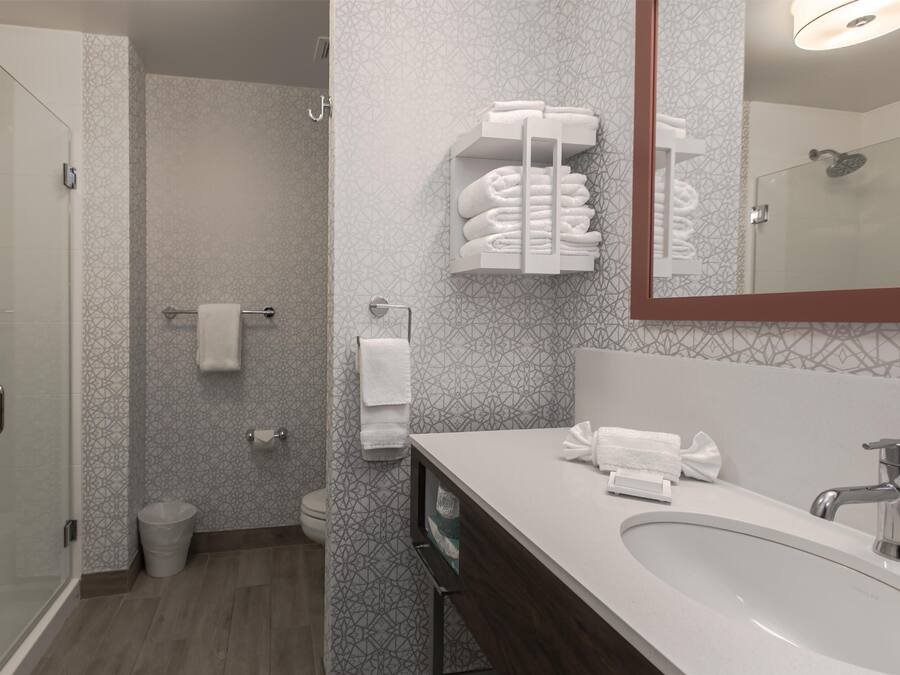 A modern bathroom with a glass shower enclosure, a white sink with a mirror, and a towel rack with neatly folded towels.
