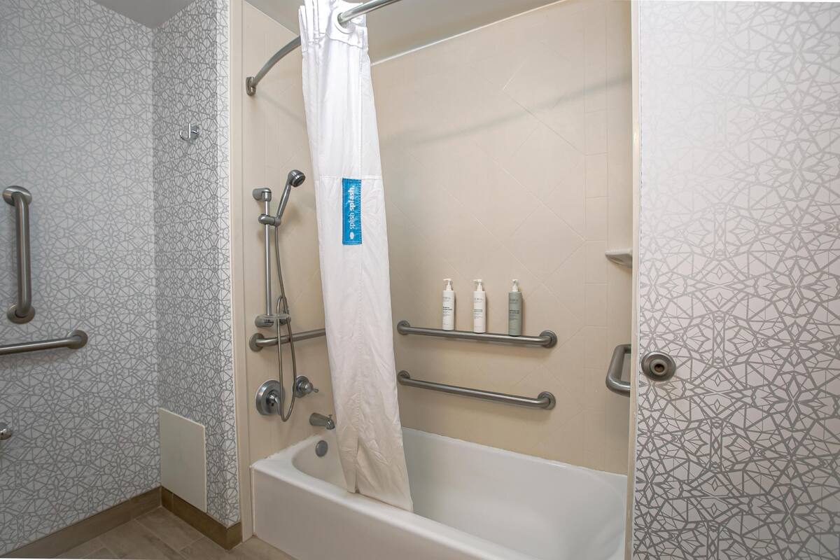 A bathroom with a bathtub, shower, and handrails.